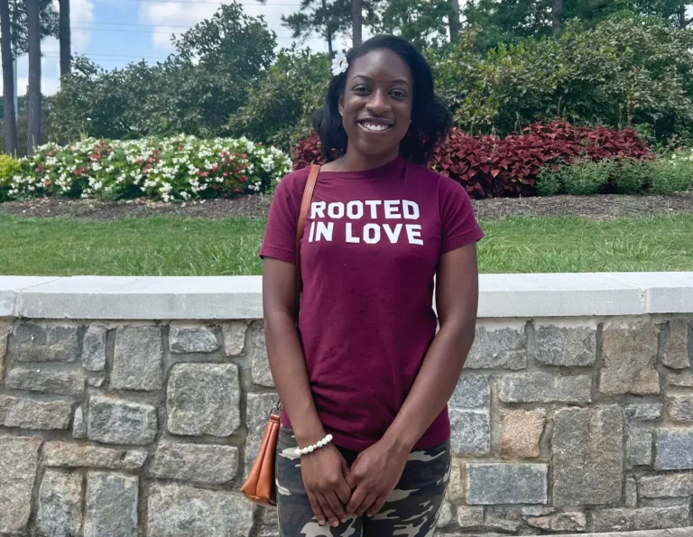 Young woman in a maroon shirt that has the words "Rooted in Love" written on it