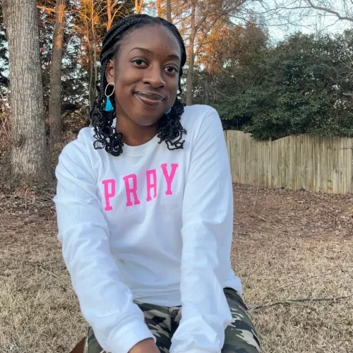 Young woman with a white shirt and the word "Pray" written on it in pink text.